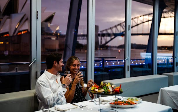 Couple enjoying dinner on a Sydney Harbour cruise with views of the Opera House and Harbour Bridge.