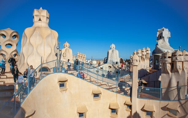Rooftop of Casa Milà in Barcelona with tourists exploring Gaudí's unique chimneys.