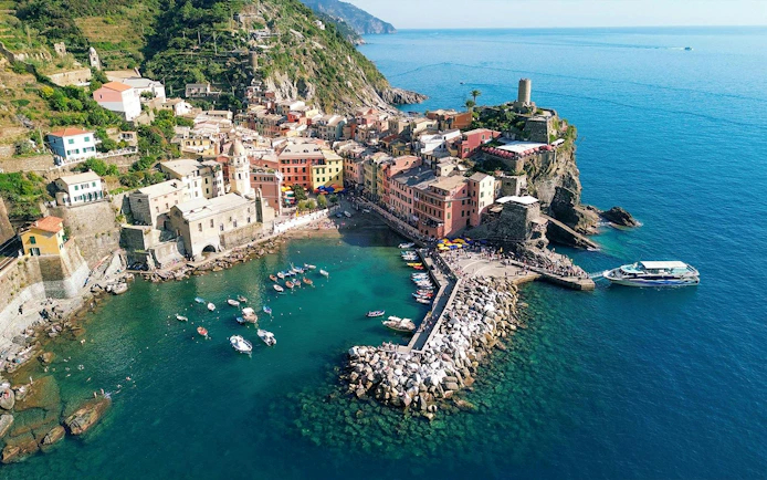 Cinque Terre coastline with colorful buildings and boats in Vernazza harbor.
