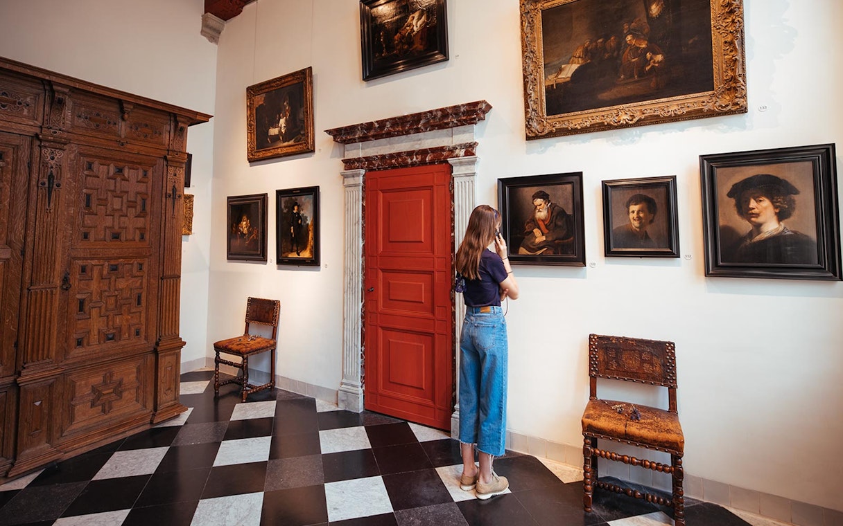Guest using audio guide at Rembrandt House Museum, viewing paintings on the wall.