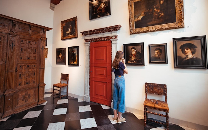 Guest using audio guide at Rembrandt House Museum, viewing paintings on the wall.