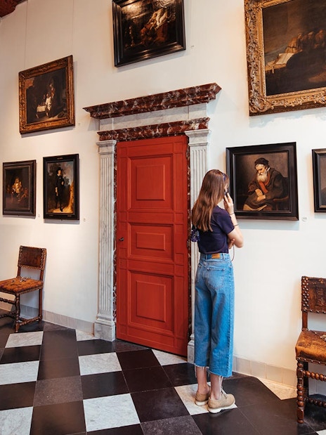 Guest using audio guide at Rembrandt House Museum, viewing paintings on the wall.