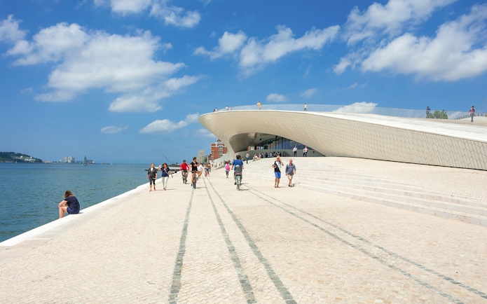 Visitors walking and cycling near the MAAT gallery along the Tagus River in Lisbon.