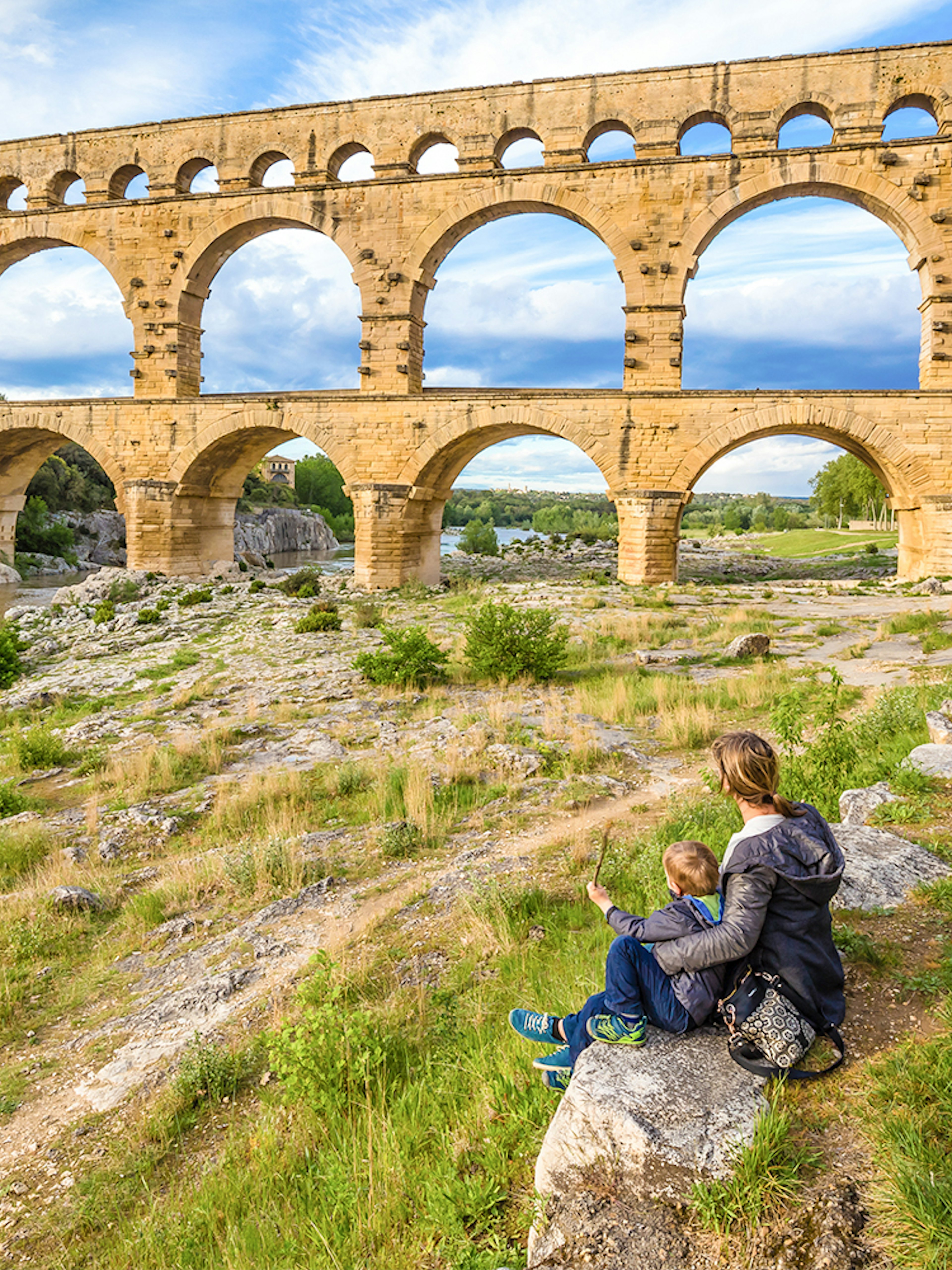 Pont du Gard aqueduct in Provence with a person and child sitting nearby.