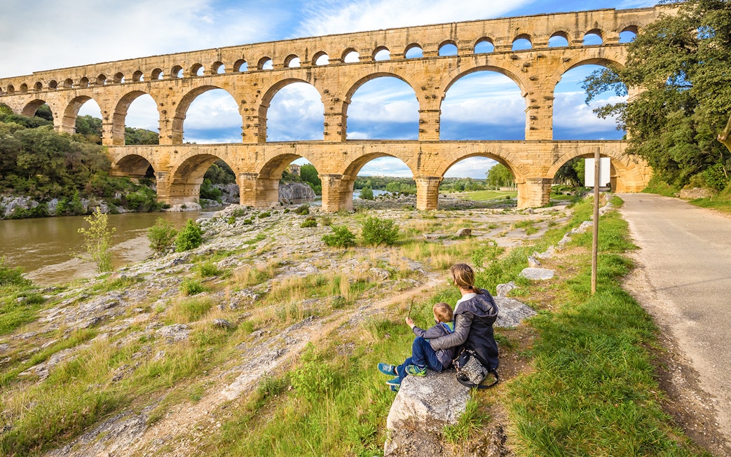 Pont du Gard aqueduct in Provence with a person and child sitting nearby.