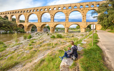 Pont du Gard aqueduct in Provence with a person and child sitting nearby.