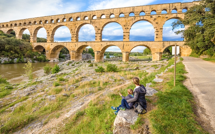 Pont du Gard aqueduct in Provence with a person and child sitting nearby.