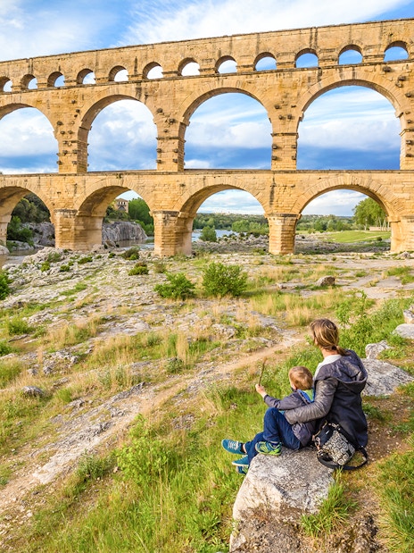 Pont du Gard aqueduct in Provence with a person and child sitting nearby.
