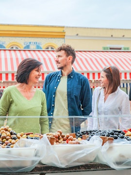 Tourists exploring a market stall with olives in Nice, France.