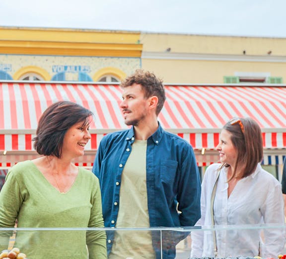 Tourists exploring a market stall with olives in Nice, France.