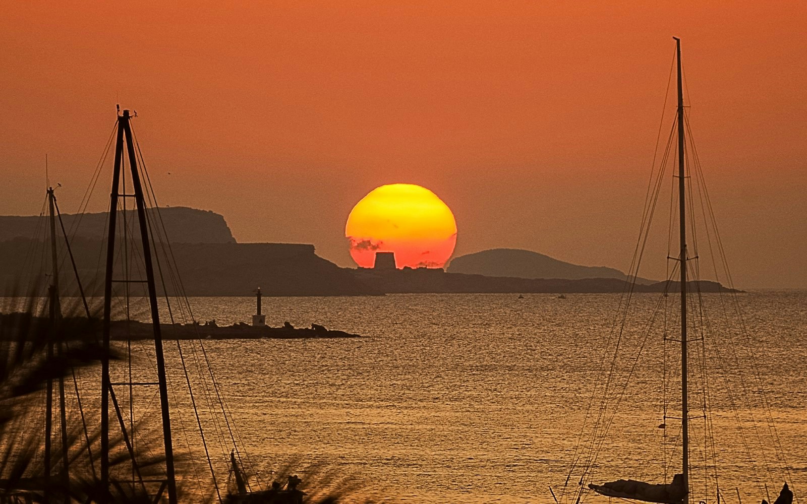 Sunset over the sea with sailboats in Sant Antoni de Portmany, Ibiza.