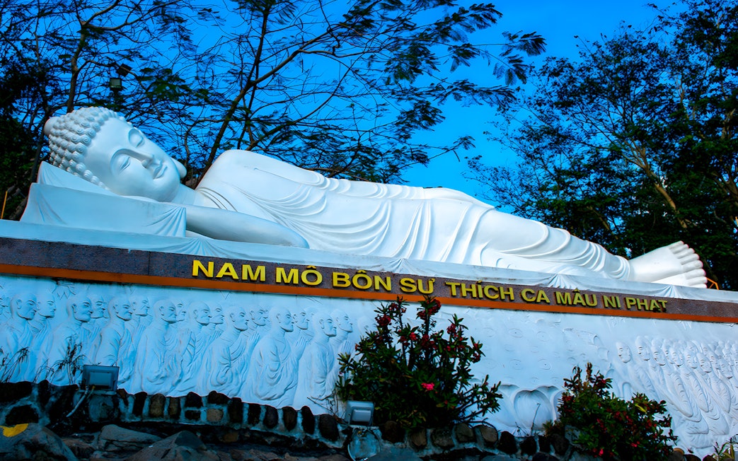 Reclining Buddha statue at Ba Den Mountain, Vietnam, surrounded by trees.