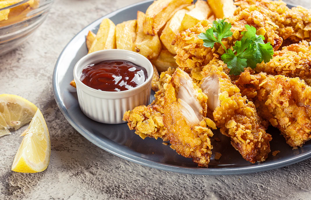 Homemade chicken nuggets with fries and dipping sauce on a plate.