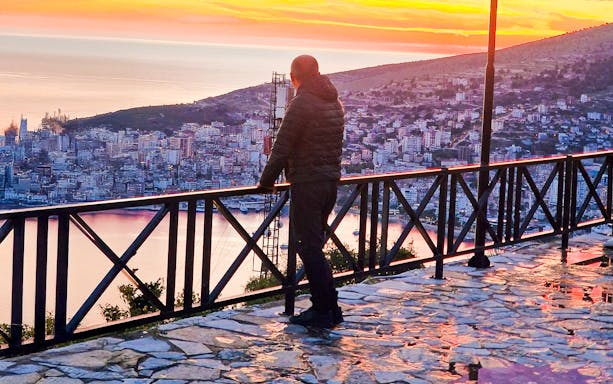 Guest admiring sunset over Sarandë from Lekursi Castle viewpoint.