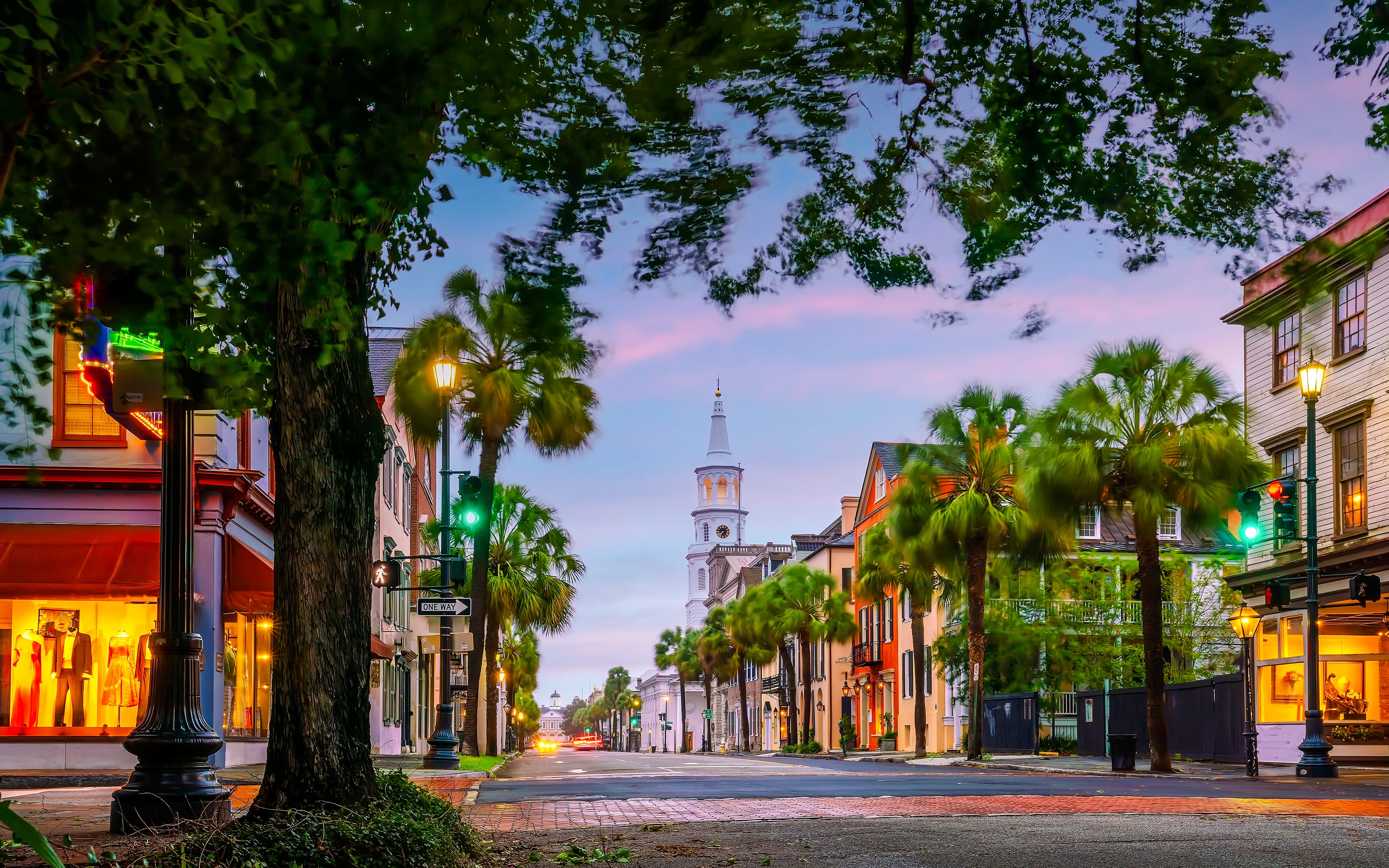 Charleston's historic downtown street with church steeple and palm trees at dusk.