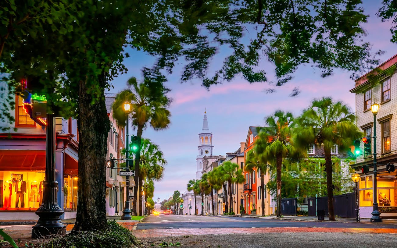 Charleston's historic downtown street with church steeple and palm trees at dusk.