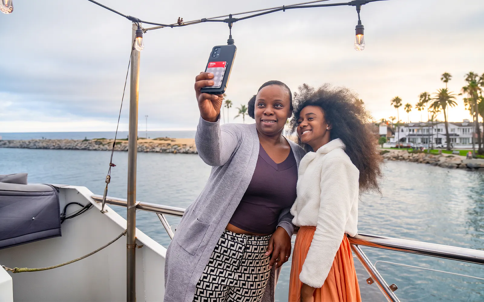 Guests taking a selfie on Newport Beach brunch cruise with ocean and palm trees in background.