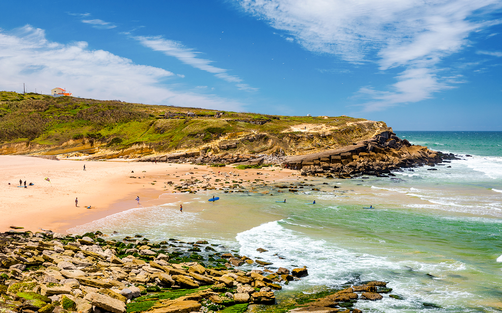 Beach near Pinhal da Nazare, Sintra, Portugal with surfers and rocky shoreline.