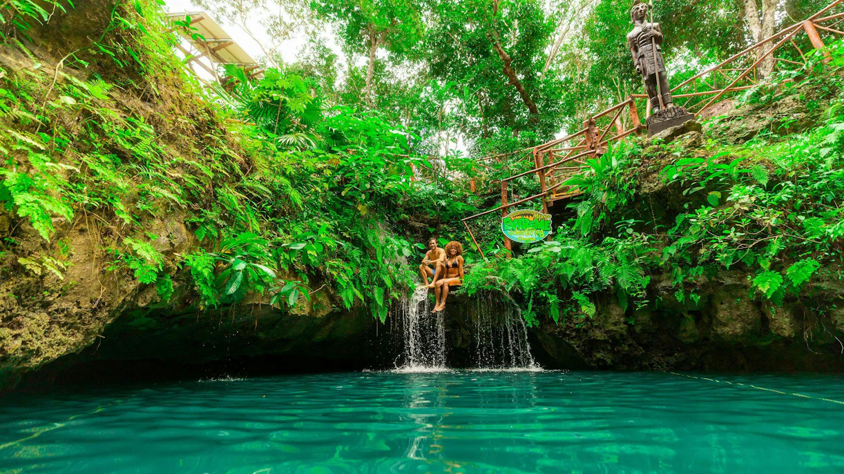 Couple sitting by a waterfall in a lush cenote, Cancun Extreme Adventure.