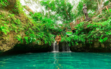 Couple sitting by a waterfall in a lush cenote, Cancun Extreme Adventure.