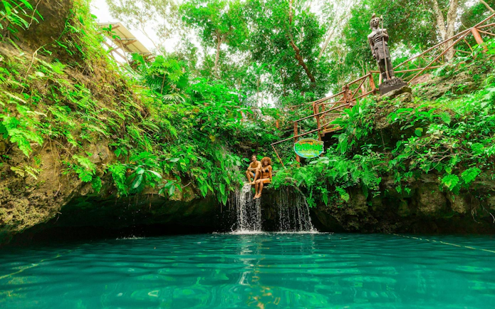 Couple sitting by a waterfall in a lush cenote, Cancun Extreme Adventure.