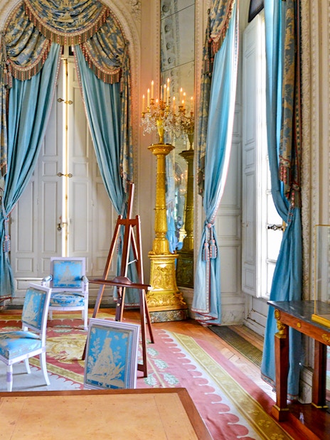 Grand Trianon room with ornate blue drapes, gilded candelabra, and elegant furniture.