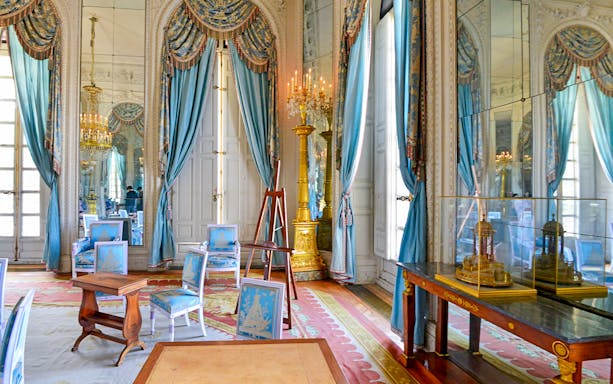 Grand Trianon room with ornate blue drapes, gilded candelabra, and elegant furniture.