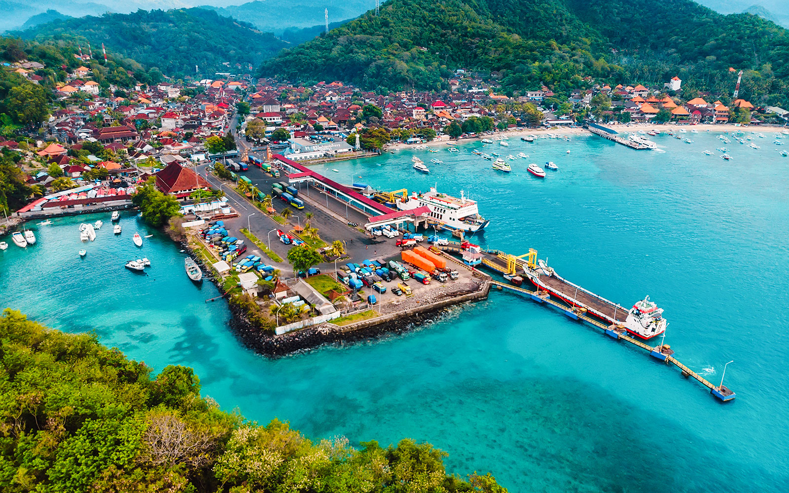 Aerial view of Padang Bai Harbor with boats and vibrant coastline in Bali, Indonesia.