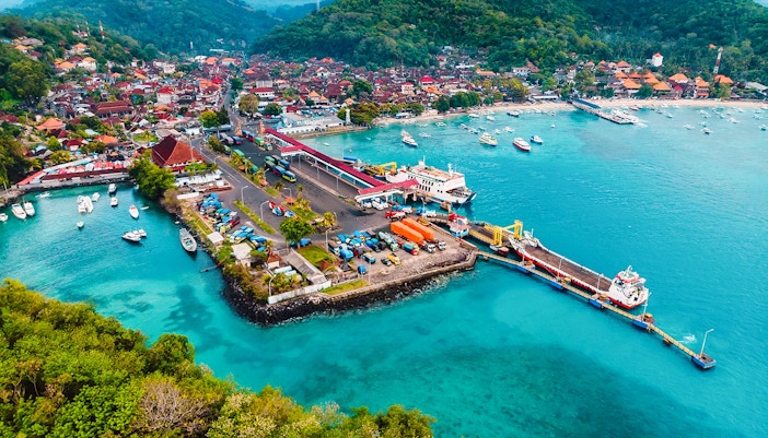 Aerial view of Padang Bai Harbor with boats and vibrant coastline in Bali, Indonesia.