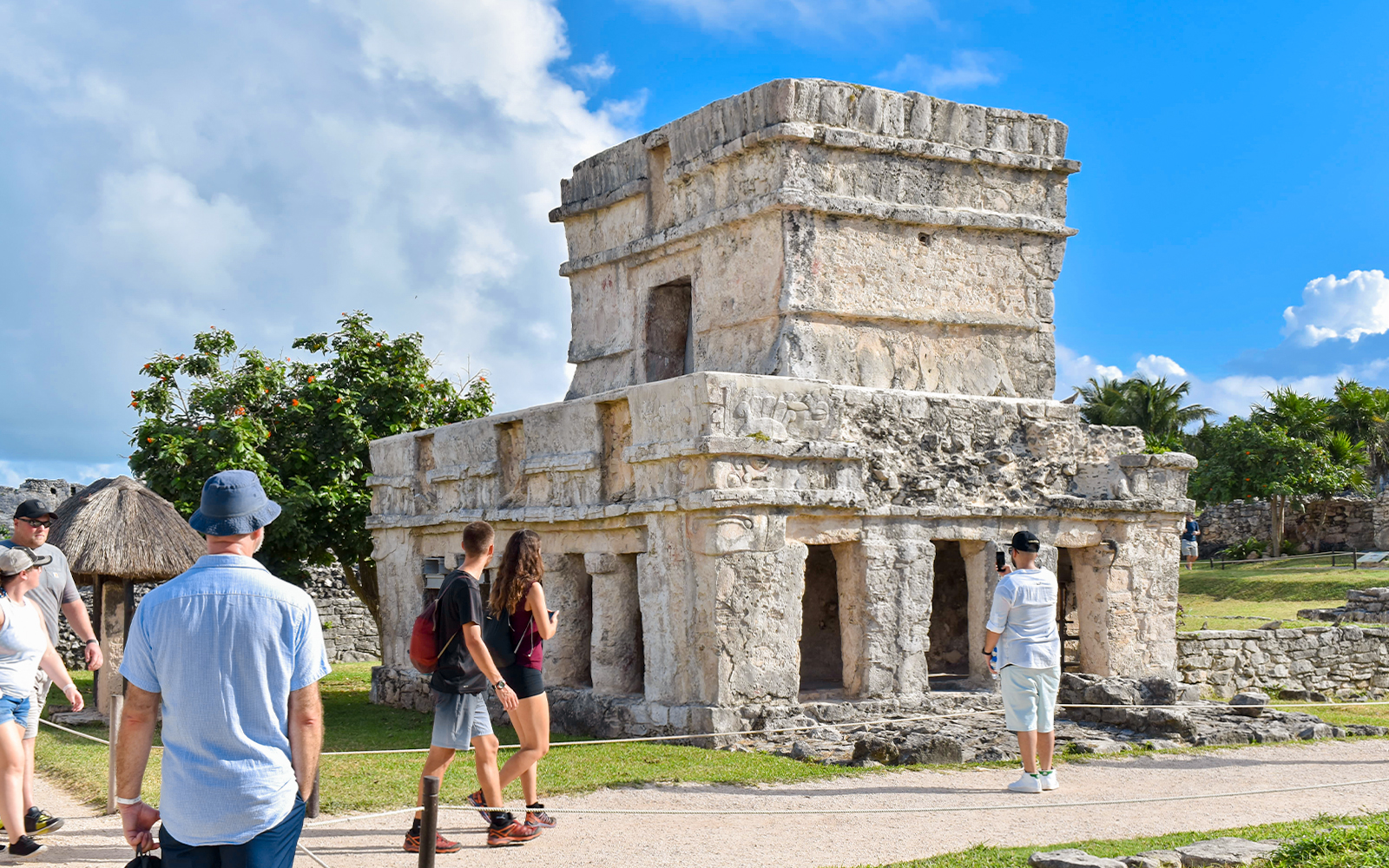 Tourists exploring ancient stone structure at Tulum ruins in Mexico.