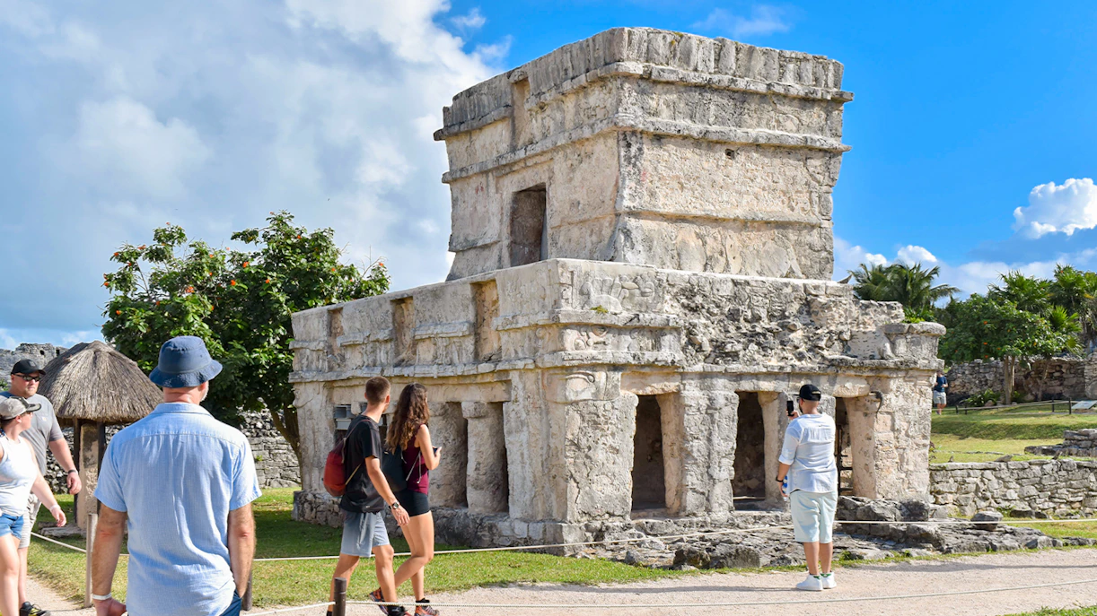 Tourists exploring ancient stone structure at Tulum ruins in Mexico.