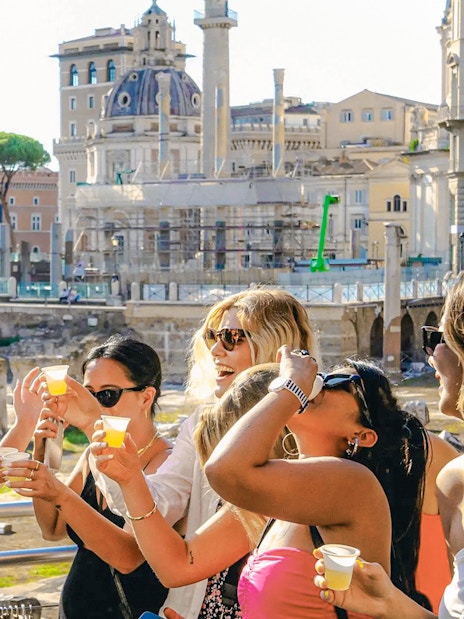 Group enjoying drinks on a Tipsy Tour in Rome with historic buildings in the background.