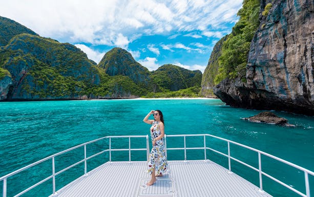 Lady on a catamaran viewing cliffs and turquoise water at Maya Bay, Thailand.