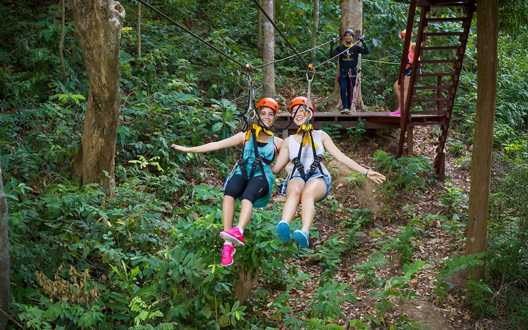 Girls ziplining through forest at Hanuman World, Thailand.