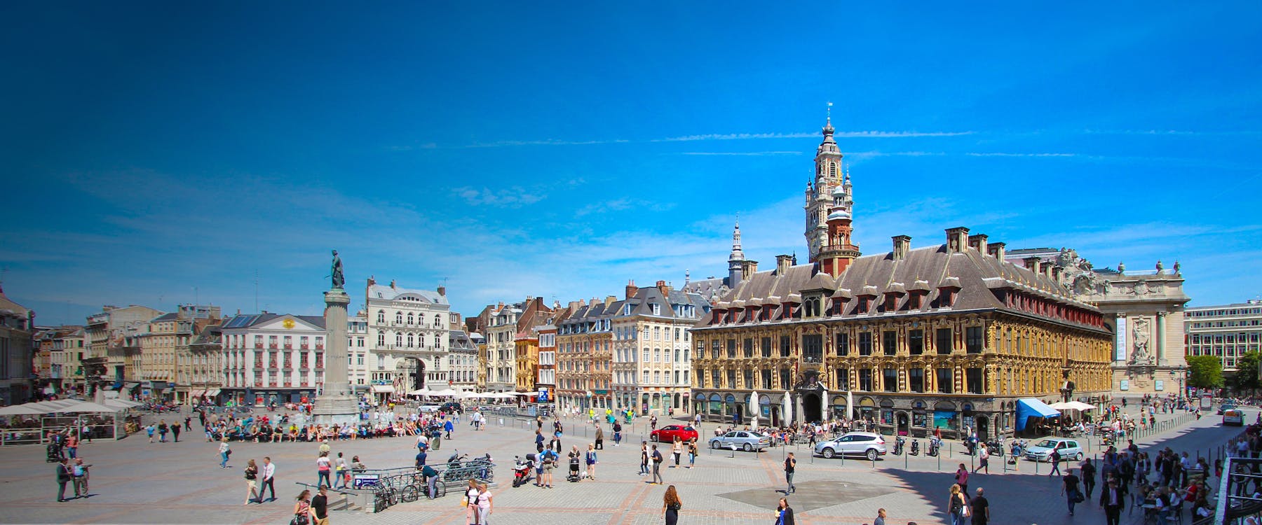 Grand Place in Lille with historic buildings and a central column under a clear blue sky.