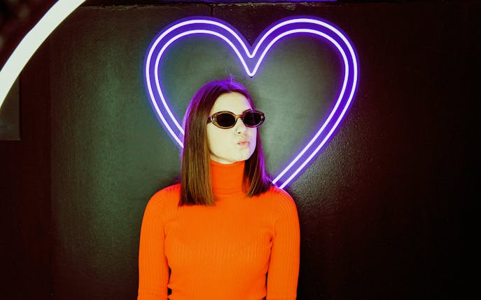 Person posing in front of neon heart at Thessaloniki Selfie Museum.