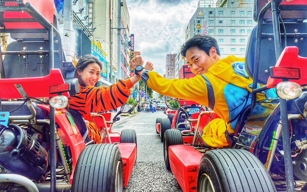 Street go-karting in Okinawa with participants in colorful costumes, high-fiving on a city road.