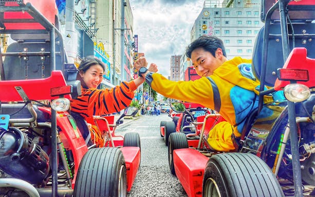 Street go-karting in Okinawa with participants in colorful costumes, high-fiving on a city road.