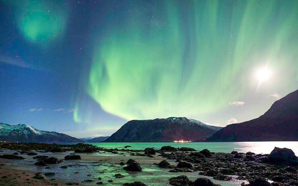 Northern Lights over Tromso fjord with mountains and shoreline.