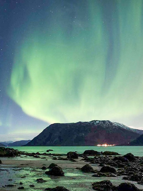 Northern Lights over Tromso fjord with mountains and shoreline.