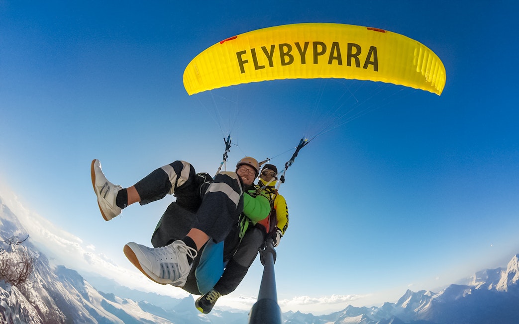 Tourist paragliding with guide over Matterhorn mountain, clear sky backdrop.