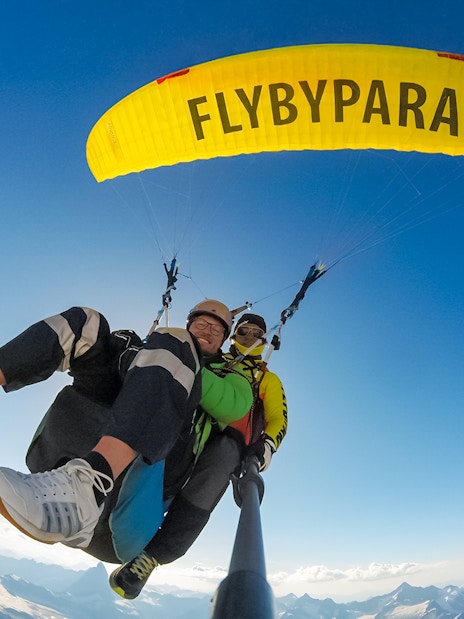 Tourist paragliding with guide over Matterhorn mountain, clear sky backdrop.