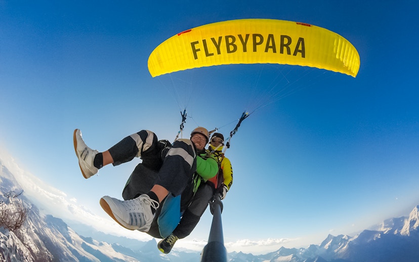 Tourist paragliding with guide over Matterhorn mountain, clear sky backdrop.