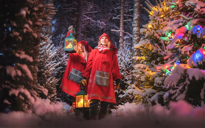 Elves in red cloaks holding lanterns in snowy forest at Elf Hat Academy, Santa's Village.