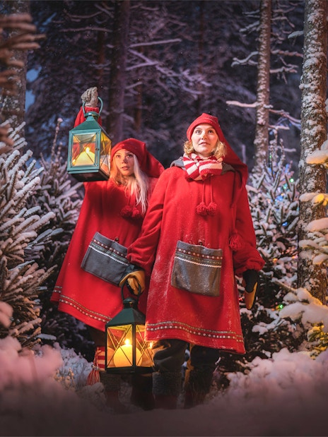 Elves in red cloaks holding lanterns in snowy forest at Elf Hat Academy, Santa's Village.
