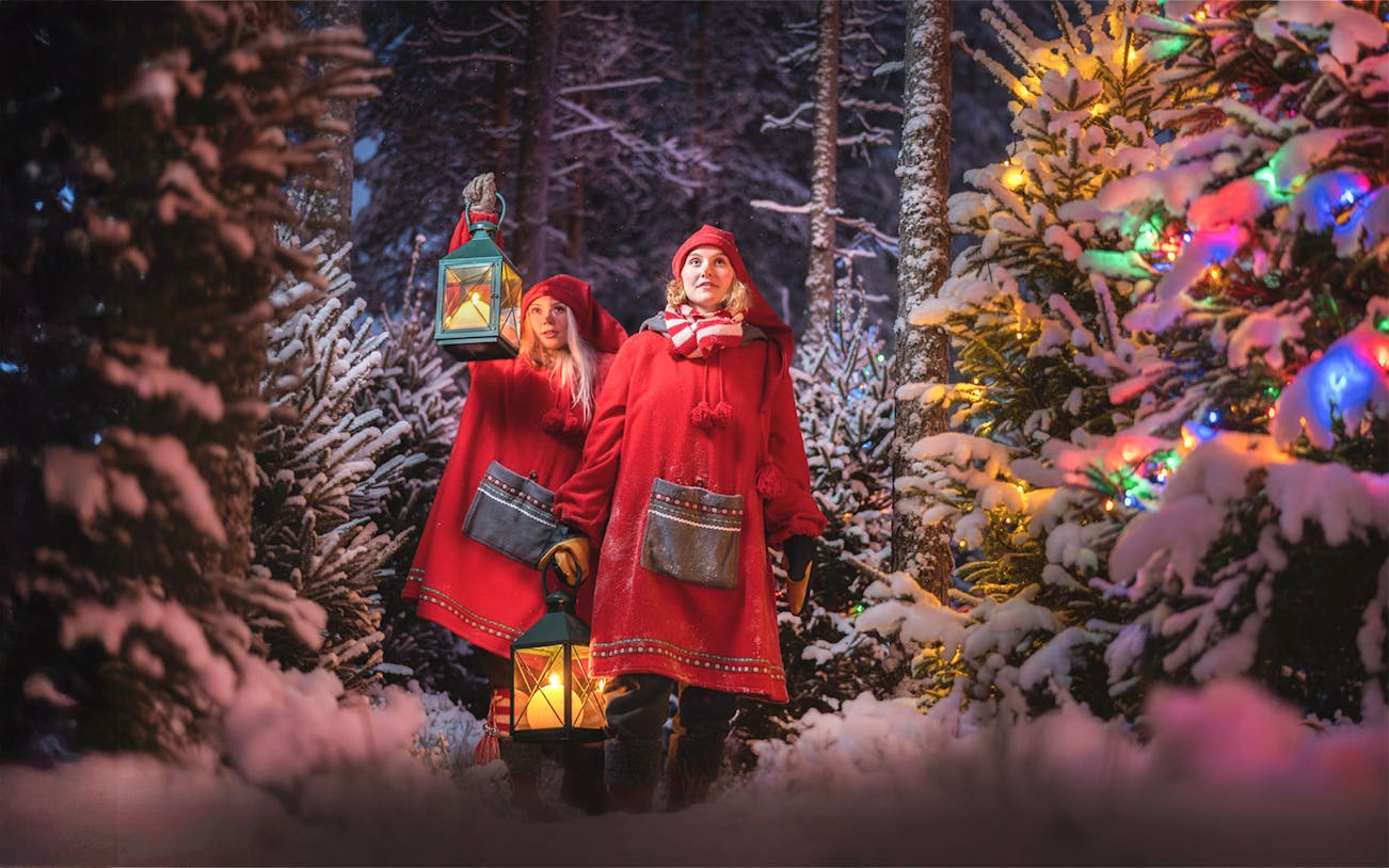 Elves in red cloaks holding lanterns in snowy forest at Elf Hat Academy, Santa's Village.