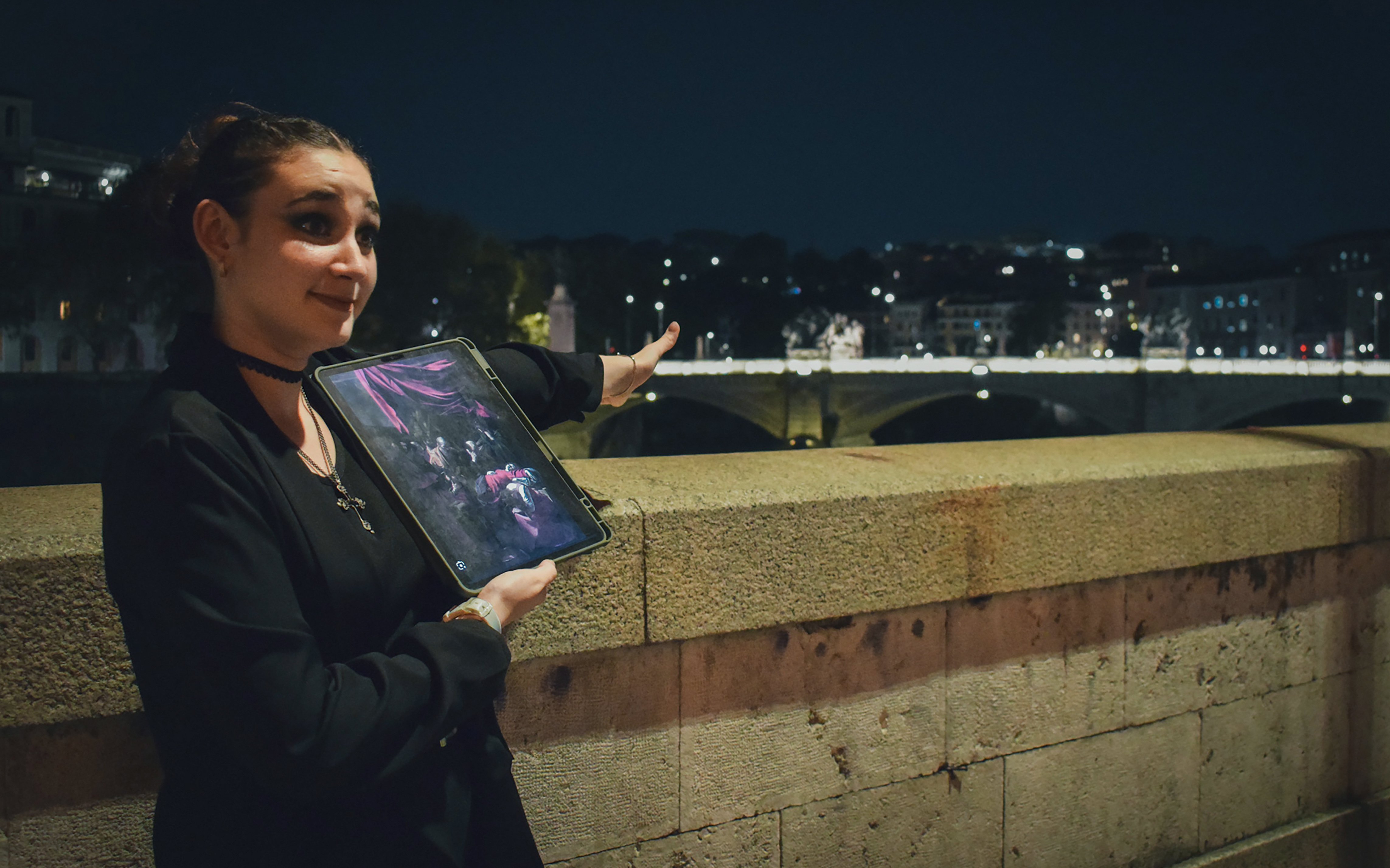 Guide presenting ghost tour details with a tablet near a lit bridge in Rome at night.