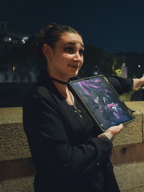Guide presenting ghost tour details with a tablet near a lit bridge in Rome at night.