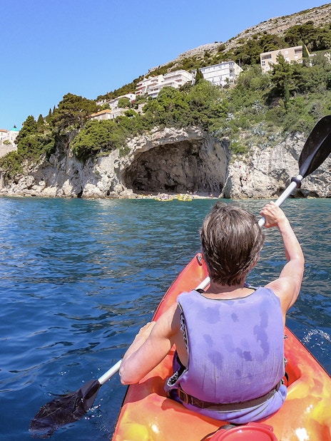 Kayaker paddling near rocky coastline in Dubrovnik during morning.
