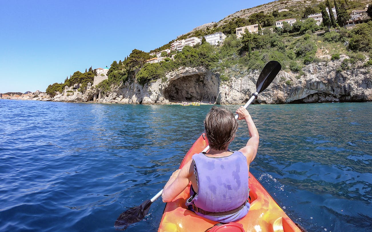 Kayaker paddling near rocky coastline in Dubrovnik during morning.